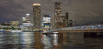 Canary Wharf night pier 2 This urban landscape photograph captures Canary Wharf Night Pier 2 in London, United Kingdom, during the evening in autumn. The image shows modern high-rise buildings of Canary Wharf with illuminated windows reflecting on the waters of the River Thames. Notable landmarks such as One Canada Square and the distinctive cylindrical Newfoundland Tower are visible among the city’s skyline. The well-lit pier structure extends out onto the River Thames, demonstrating the urban architecture that characterizes this financial district in London.